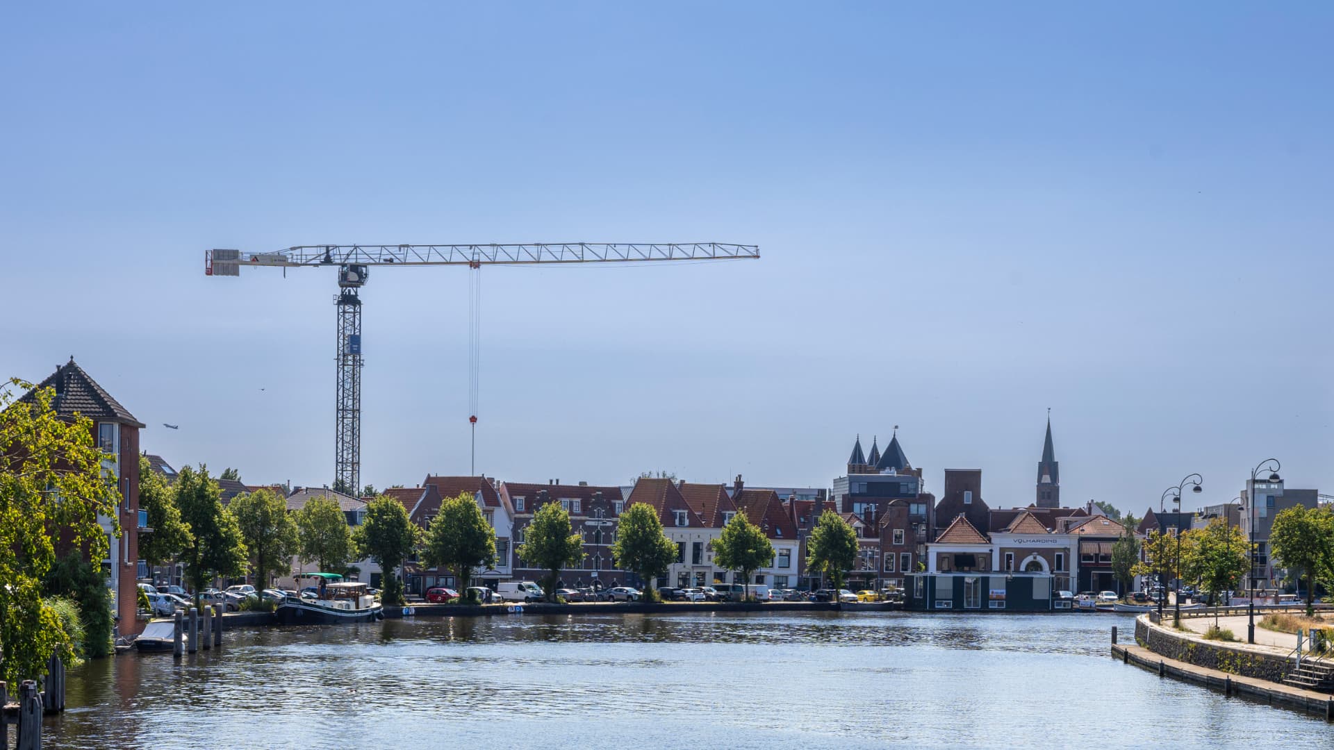 Zicht over het Spaarne in Haarlem, met kadehuizen, bomen en een bouwkraan in de skyline.